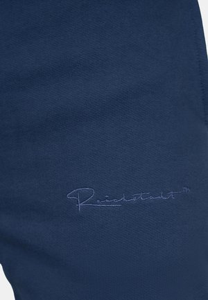 Marineblauw stof met een gladde textuur, voorzien van geborduurd handtekeningdetail. Close-up van kledingmateriaal en branding.