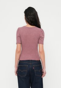 Μοβ πλεκτό τοπ με ριμπ ύφασμα, κοντά φουσκωτά μανίκια και σκιασμένη τελείωμα, συνδυασμένο με σκούρο τζιν παντελόνι που διαθέτει πίσω τσέπες και λεπτομέρειες ραφής.