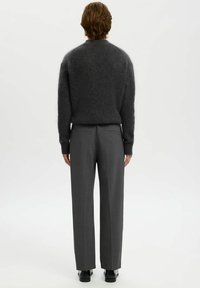 Grauer, flauschiger Pullover mit rundem Ausschnitt, kombiniert mit grauen, maßgeschneiderten Hosen. Die Beine sind gerade geschnitten und die Schuhe sind schwarz.