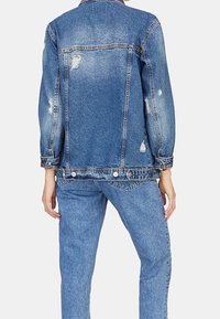 Spijkerjasje in lichtblauw met distressed details, knoopsluitingen en een ontspannen pasvorm, gecombineerd met bijpassende lichtblauwe jeans.