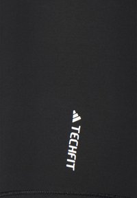 Musta urheilupaita, joka on valmistettu sileästä ja joustavasta materiaalista, valkoisella "TECHFIT"-logolla ja huomaamattomilla ompeluyksityiskohdilla.