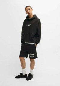 Ensemble de sweat à capuche noir et de shorts avec un logo sur le devant et des accents à carreaux ; fabriqué en matériau doux avec une coupe décontractée.