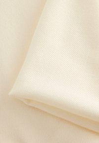 Tkanina w kolorze kremowym o fakturze, z delikatnym wzorem prążków, złożona w taki sposób, aby pokazać jej gładką powierzchnię i lekki połysk.