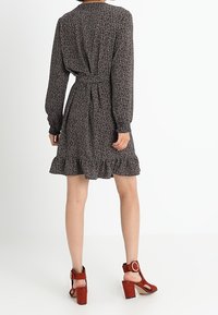 Robe noire à fleurs avec des manches longues, taille cintrée et ourlet volanté. Associée à des sandales à talons blocs striées marron.