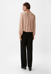 Jasnoróżowa bluzka z długim rękawem, z marszczonym dekoltem i elastycznymi mankietami, w połączeniu z czarnymi spodniami szerokimi w nogawkach oraz sandałami na obcasie.