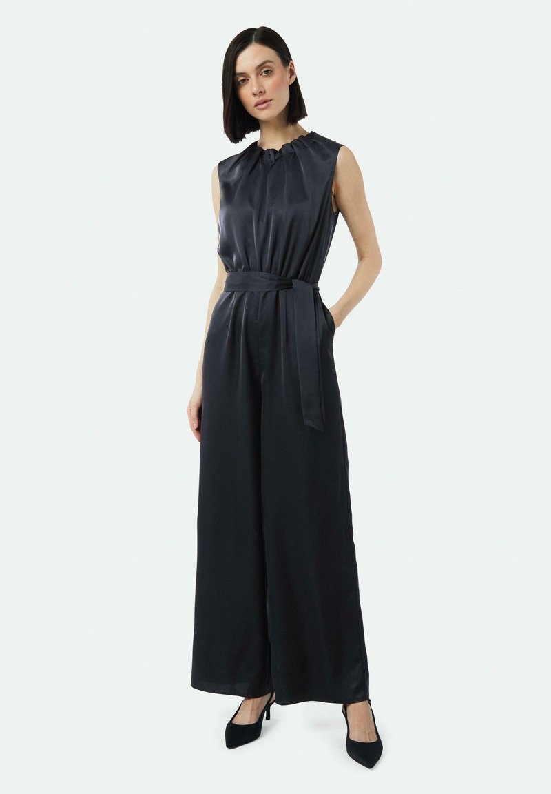 Mouwloze zwarte jumpsuit met een verzamelde halslijn, wijde pijpen en een gestrikt tailleband. Glad, glanzende stofafwerking.