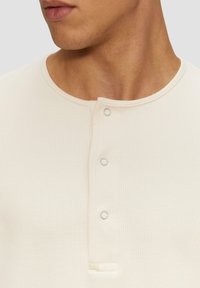 Licht crèmekleurig, geribbeld henley-shirt met een ronde halslijn, drie zilveren drukknoopsluitingen bij de pat en een kleine gestikte accent.