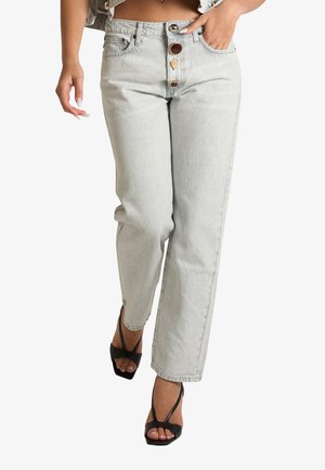 Donna che indossa jeans grigio chiaro a vita alta e gamba dritta con tre bottoni decorativi e sandali neri con tacco e punta aperta.