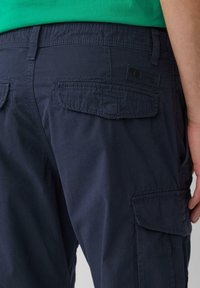 Pantalons cargo marine en tissu texturé avec deux poches latérales et des coutures décoratives, comportant un badge logo sur la poche arrière.