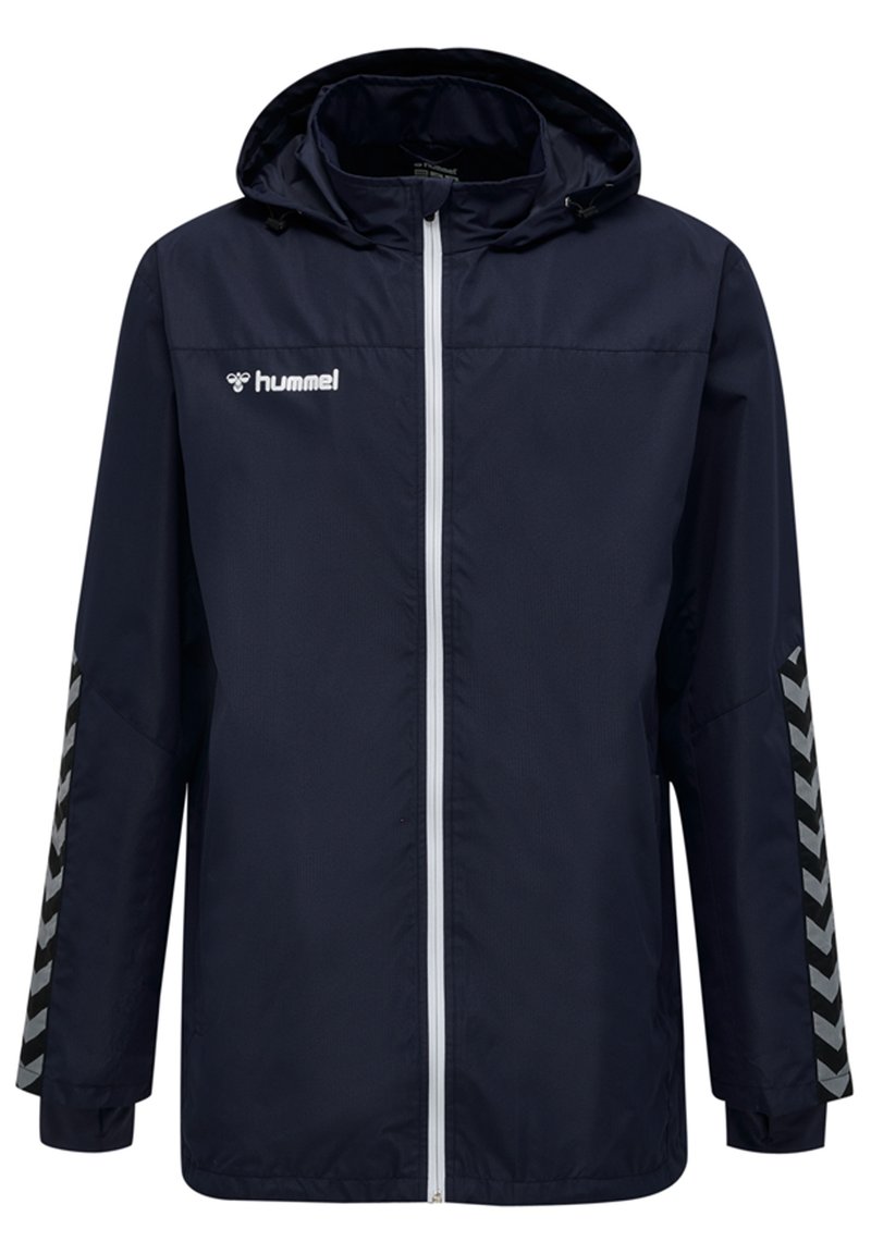 Marinblå vindjacka med huva, vit dragkedja och Hummel-logotyp. Har svarta chevronmönster detaljer på ärmarna. Lätt material.