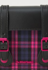 Černá kožená taška s klopou z růžové kostkované látky, s růžovými prvky a prošíváním, a výrazným logem "Dr. Martens".