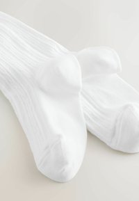 Valged puuvillased sokid soonilise tekstuuri ja tugevdatud varbaosaga, klassikalise disaini ja sileda viimistlusega.