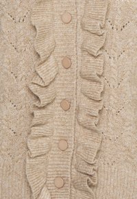 Strickjacke in Beige mit strukturiertem Muster, versehen mit einem Rüschensaum entlang der Knopfleiste und runden, neutralfarbenen Knöpfen.