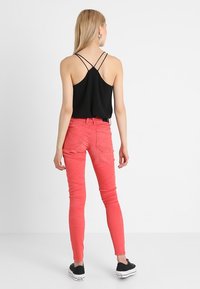 Top negro sin mangas con tirantes cruzados, combinado con jeans ajustados rosas y zapatillas de lona negras. Tela suave, corte ajustado, sin patrones visibles.