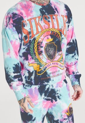 Tie-Dye Sweatshirt und Sweatpants in Pastellblau, Pink und Lila mit orangefarbenem SIKSILK-Logo und Wappen-Design, getragen von einer tätowierten Person.