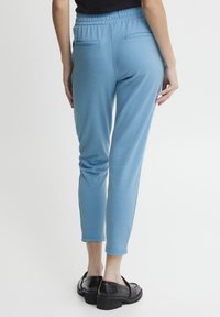 Joggers bleu clair, fuselés, avec une taille élastique, deux poches arrière et une texture douce, associés à des chaussures à plateforme noires.