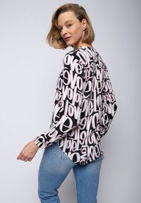 Blouse à manches longues en tissu noir avec un motif de texte "love" en blanc et rose. Légère, coupe décontractée, avec un ourlet arrondi et des poignets standards.