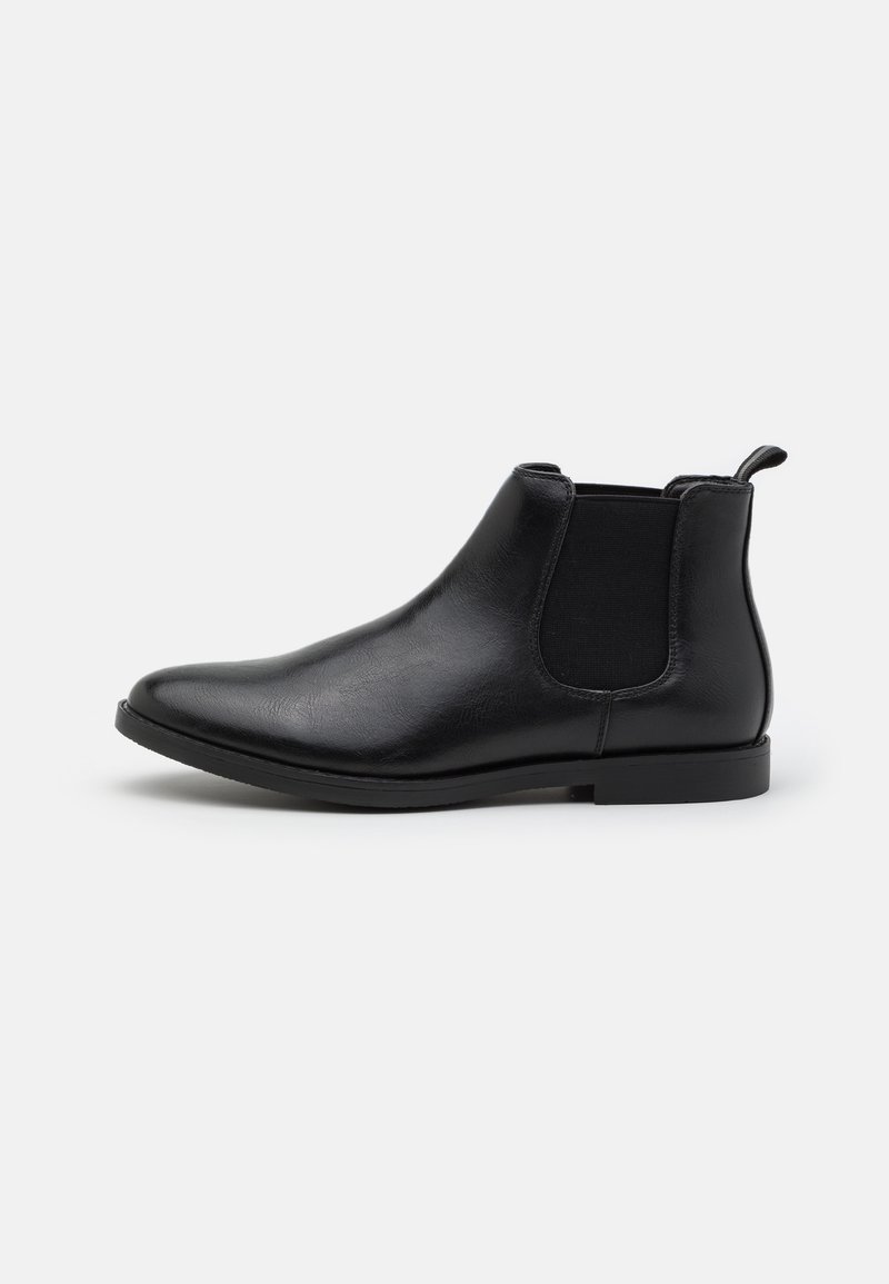 Botín Chelsea de cuero negro con paneles elásticos a los lados, tacón bajo, punta redondeada y un asa en la parte trasera. Textura suave y diseño elegante.