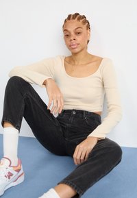 Maglietta a maniche lunghe a coste color crema abbinata a jeans neri a vita alta. Sneakers bianche e rosa e calzini bianchi alla caviglia completano l'outfit.