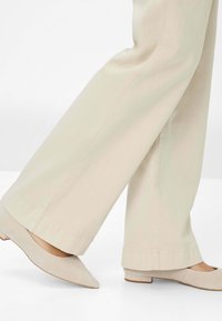 Beige wijde stoffen broek met een gladde textuur, gecombineerd met lichtbeige puntige ballerina's met een lage hak en subtiele stikseldetails.