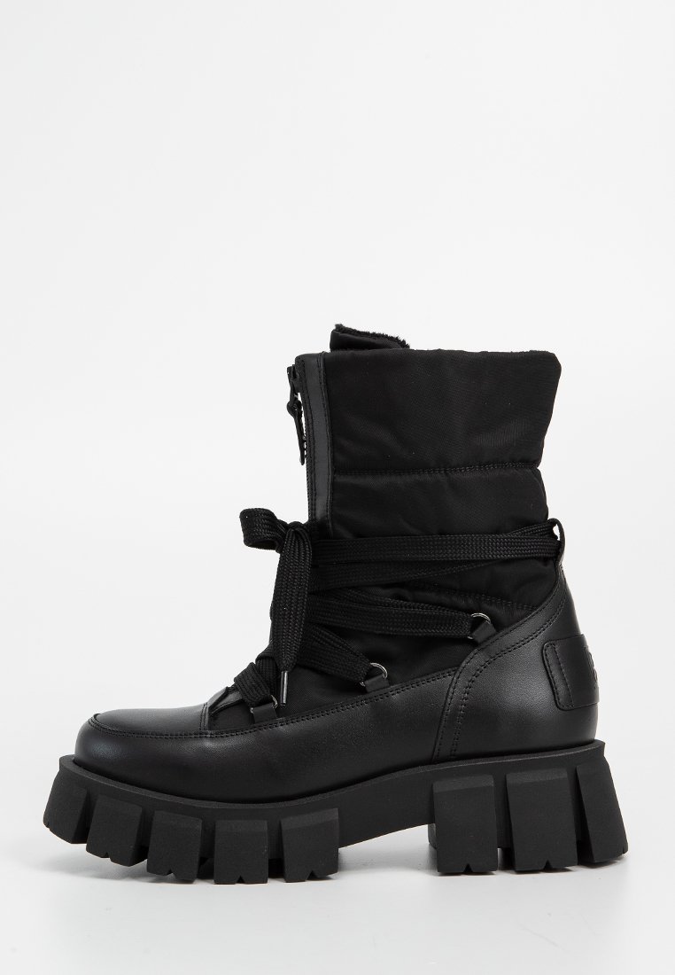 Schwarze Knöchelstiefel bestehen aus einer Mischung aus Leder und Stoff und sind mit Schnürsenkeln und einem Reißverschluss gesichert. Dicke, klobige Sohlen bieten Stabilität.