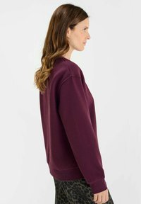 Dark purple sweatshirt with a relaxed fit, ribbed cuffs, and a round neckline, paired with patterned pants featuring a leopard print.