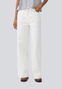 Pantalon large blanc avec une taille à cordon de serrage et des poches latérales, fabriqué dans un tissu texturé. Assorti avec un top court gris.