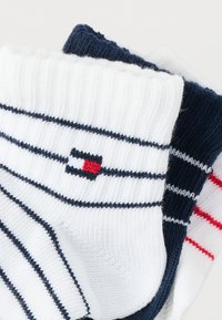 Ζεύγος κάλτσες, μία λευκή με ναυτικό μπλε ρίγες και λογότυπο, η άλλη ναυτικό μπλε με αντίθετες ρίγες σε λευκό και κόκκινο, κατασκευασμένες από μαλακό ύφασμα.