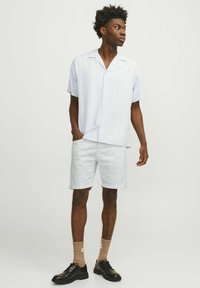 Camisa de manga corta azul claro, pantalones cortos blancos, zapatos negros y calcetines beige. La camisa tiene un corte relajado con cuello y botones.