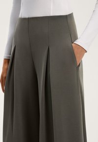 Ciemnoszare, szerokie spodnie z gładką teksturą i bocznymi kieszeniami, z fałdami z przodu i wysokim stanem, zestawione z białą bluzką z długim rękawem.