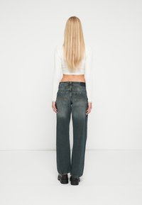 Jeans cinzentos claros de perna larga com tecido texturizado e costuras visíveis. A parte de trás apresenta dois bolsos e um fecho de correr.