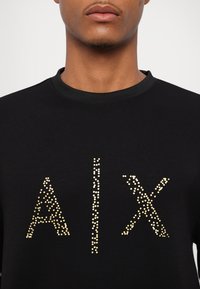 Sudadera negra con un diseño de puntos dorados formando la palabra "AIX" en el frente, con un cuello redondo y tejido texturizado.