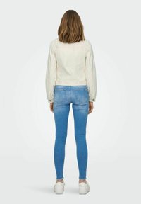 Light beige denim jacket with long sleeves, paired with blue skinny jeans and white sneakers. The jacket features a structured design and back seams.