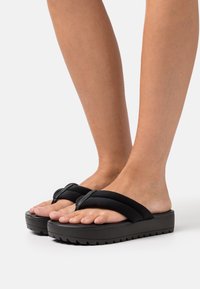 Mustat korokepohjasandaalit, joissa on pehmeä tekstuuri hihnat, leveä varvastila ja paksu, uritettu pohja pitoon. Kevyt muotoilu mukavuutta ja helppoutta varten.