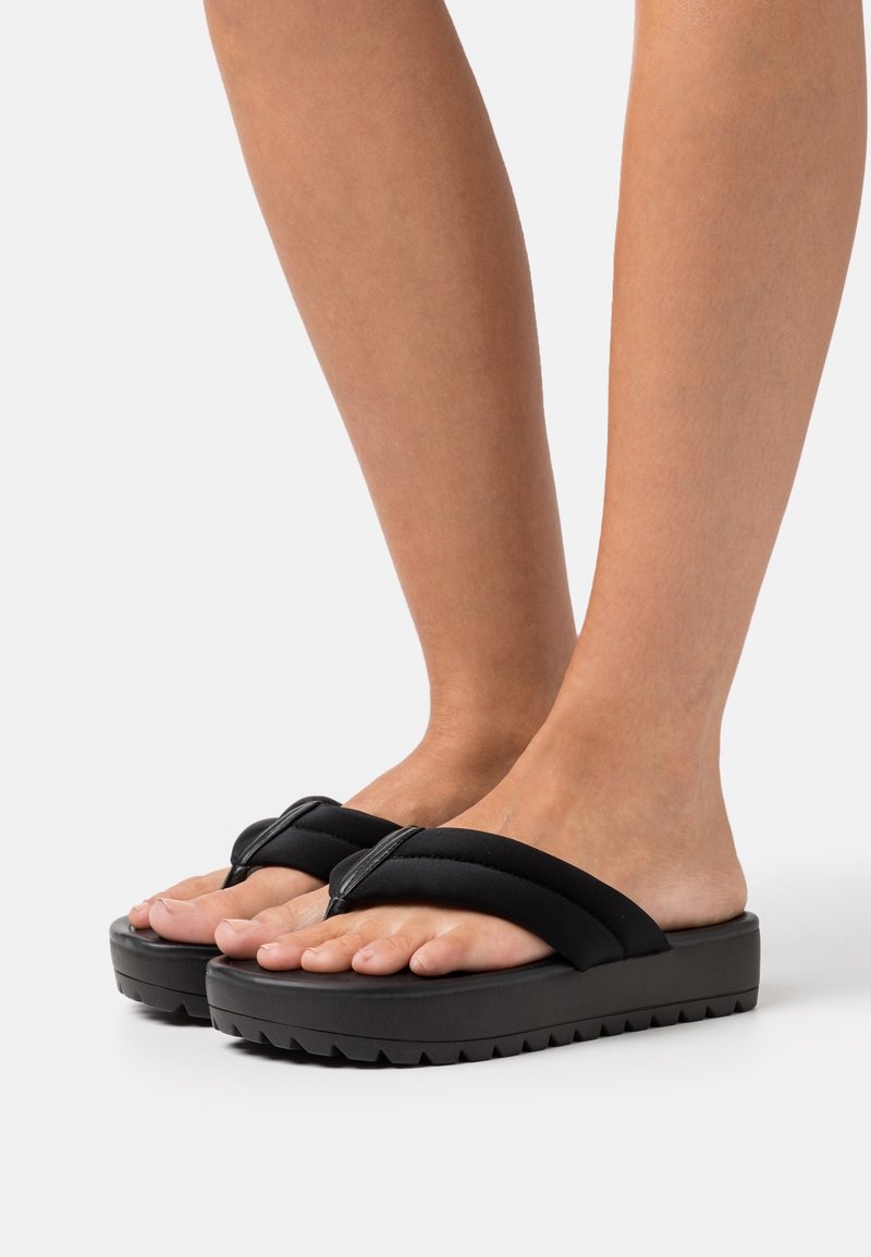 Mustat korokepohjasandaalit, joissa on pehmeä tekstuuri hihnat, leveä varvastila ja paksu, uritettu pohja pitoon. Kevyt muotoilu mukavuutta ja helppoutta varten.