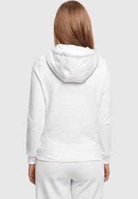 Witte katoenen hoodie met een zachte textuur, voorzien van een capuchon, lange mouwen en een ontspannen pasvorm die zichtbaar is aan de achterkant.