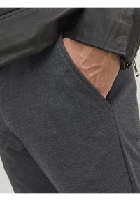 Grå, texturerade tygbyxor med en sidficka, kombinerade med en svart läderjacka. Närbild på tyget och hand i fickan.