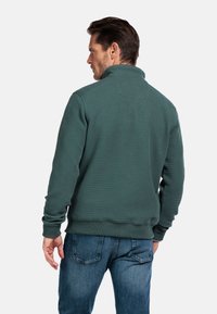 Groene textuurpullover met een hoge kraag, met een effen kleur en geribde manchetten, gedragen met blauwe denimjeans.