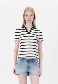 Randig stickad polo skjorta i vitt med svarta ränder, utrustad med svart krage och korta ärmar. Bärs med urblekta jeansshorts.