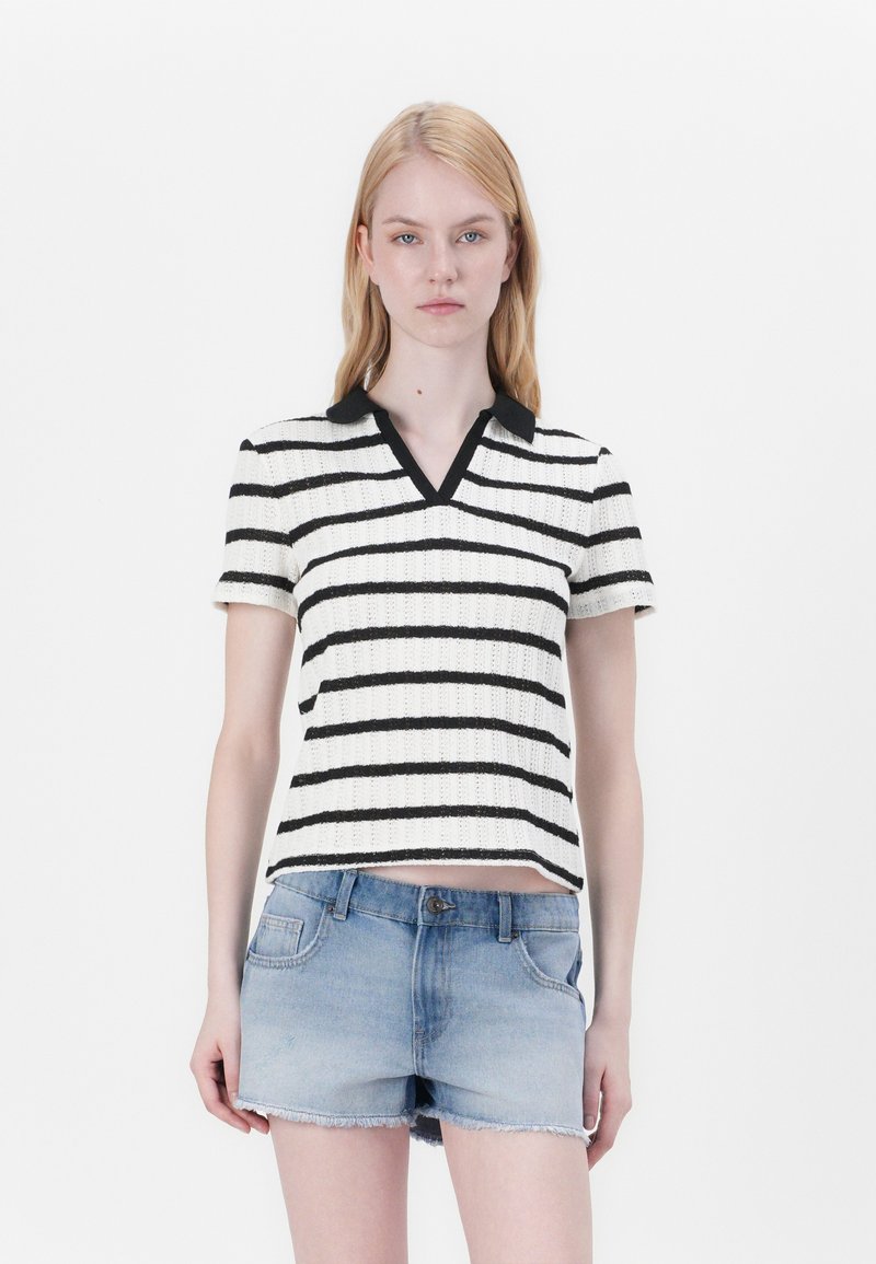 Randig stickad polo skjorta i vitt med svarta ränder, utrustad med svart krage och korta ärmar. Bärs med urblekta jeansshorts.
