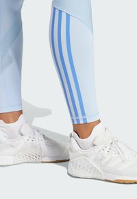 Lyseblå trænings leggings med teksturerede paneler og tre lodrette striber, parret med hvide sneakers featuring mesh og teksturerede detaljer.