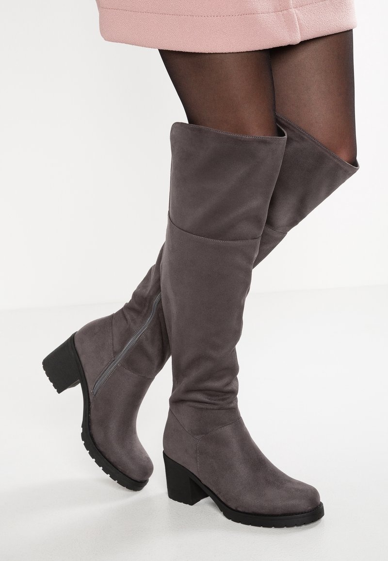 Graue Fake-Suede Overknee-Stiefel mit Blockabsatz, ausgestattet mit einem Reißverschluss an der Seite und einer glatten Textur, kombiniert mit schwarzen Strumpfhosen.