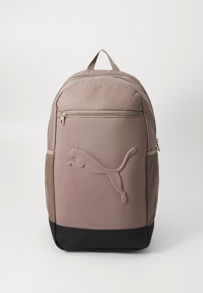 Mochila de tecido castanho com um logo Puma texturizado. Apresenta um bolso frontal, bolsos laterais em malha e um painel inferior preto. Fecho com zíper.