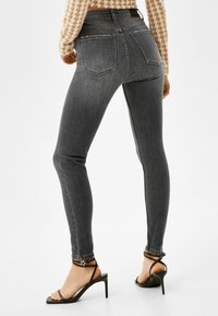 Vaqueros de mezclilla gris de talle alto y corte ajustado con una textura suave, que cuentan con dos bolsillos traseros y detalles de costura. Combinados con tacones negros de tiras.