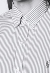 Skjorta med vertikala ränder och knäppning, delvis knäppt, med en liten broderad polo-spelare logotyp i nedre högra hörnet.