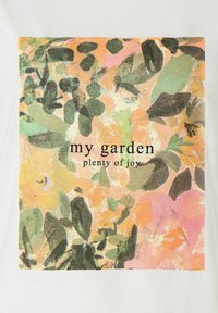 White t-shirt featuring a square graphic print with green and orange foliage patterns and the text "my garden plenty of joy" in black.