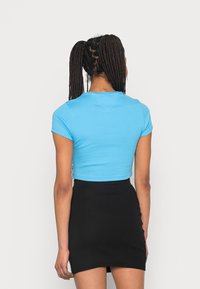 Lyhythihainen, lyhennetty sininen toppi pyöreällä kaula-aukolta, yhdistettynä ribattu musta hame. Tasainen kangas, mukautettu muotoilu ja yksivärinen väriteema.