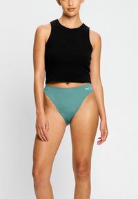 Haut court sans manches noir avec un col rond, associé à un bas de bikini taille haute teal comportant un petit logo blanc sur le côté.