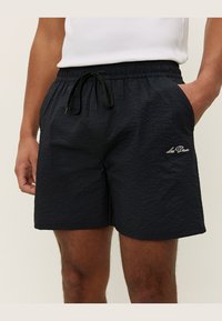 Svart teksturert badeshorts med elastisk livbånd, justerbar snor og sidelommer; har brodert logo på venstre bein.