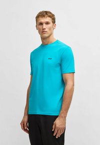 Turquoise short-sleeve t-shirt made of cotton, featuring a round neckline and a small black logo on the chest. Simple design, smooth texture.